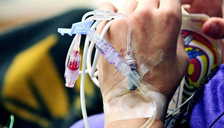 A young child has an IV running into their hand in the hospital