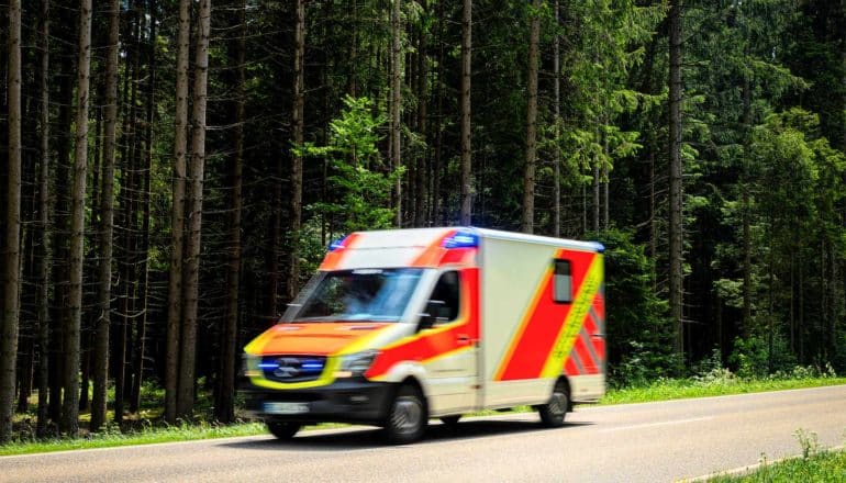 An ambulance drives down a road through a forest