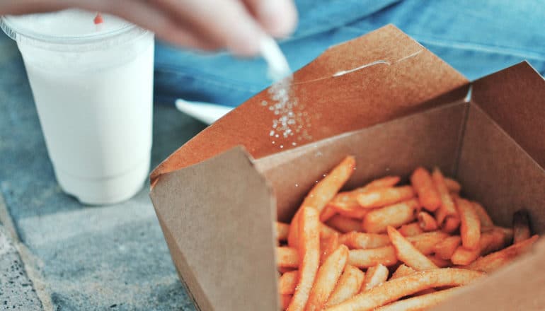 hand puts salt on fries