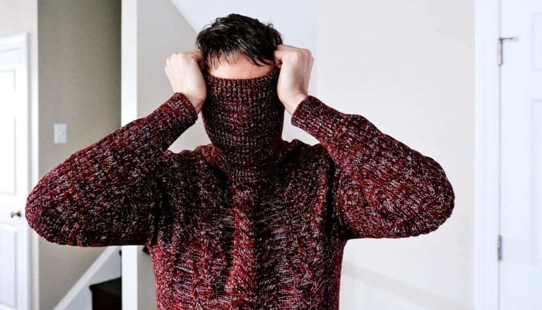 A man pulls his red sweater's collar over his face