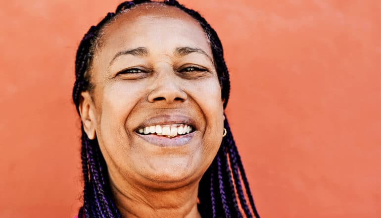 A smiling woman takes a selfie against an orange wall