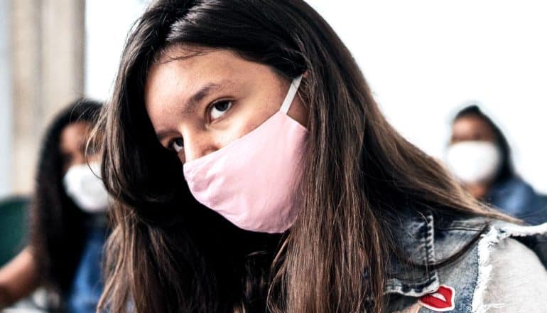 A young woman sits in class wearing a pink face mask