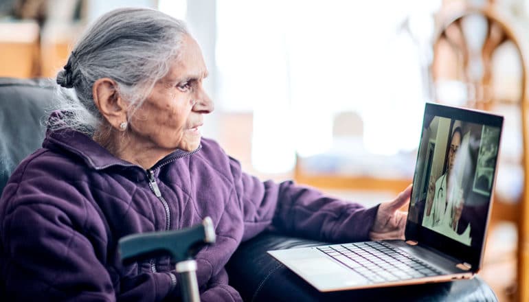 A woman speaks to a doctor via a telehealth platform on a laptop