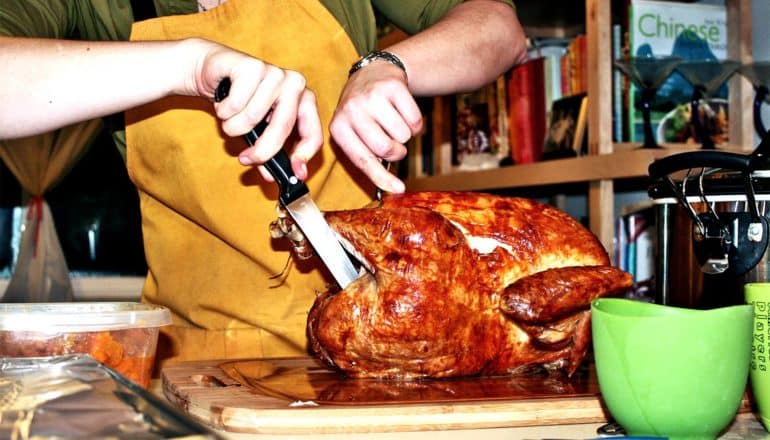 A person carves a turkey while wearing a yellow apron