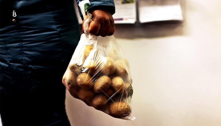 A woman at a food pantry holds a plastic bag of yellow potatoes