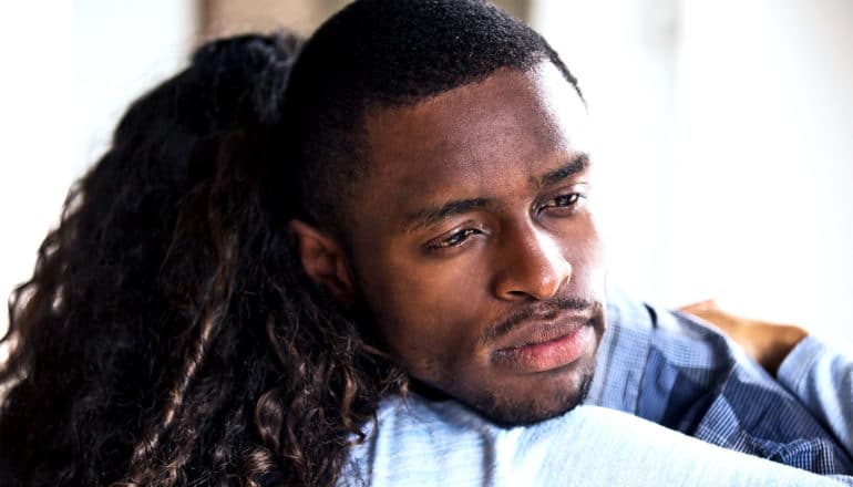 A man hugs a woman while looking lost in thought