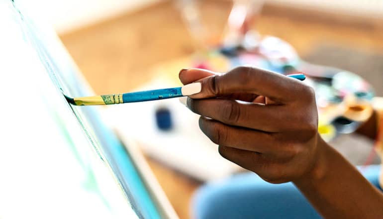 A young woman paints on a canvas with a blue brush