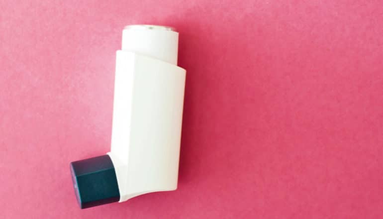 An asthma inhaler sits on pink construction paper