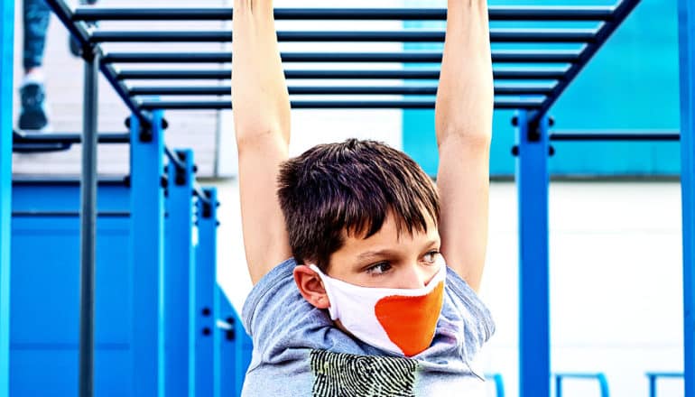 A young boy hangs from monkey bars at a park outdoors