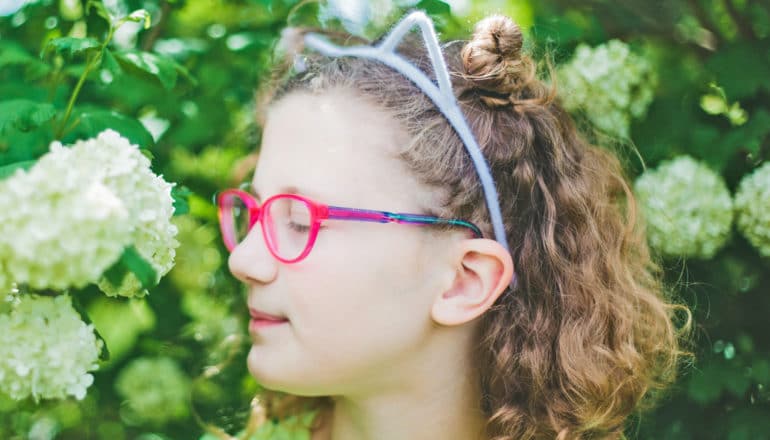 kid in neon glasses and cat headband smells hydrangea