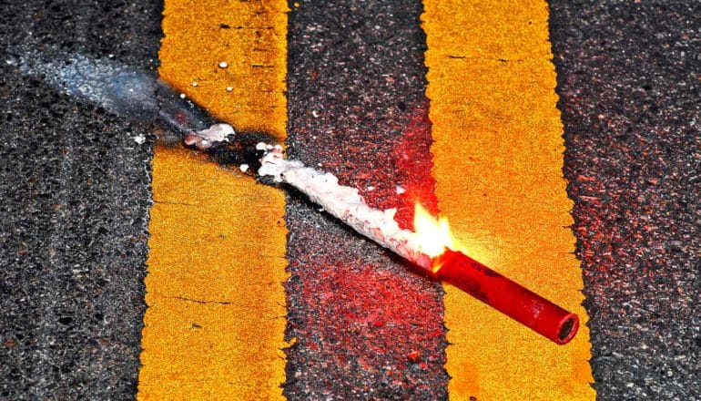 A road flare burns while sitting on two solid yellow lines on a road