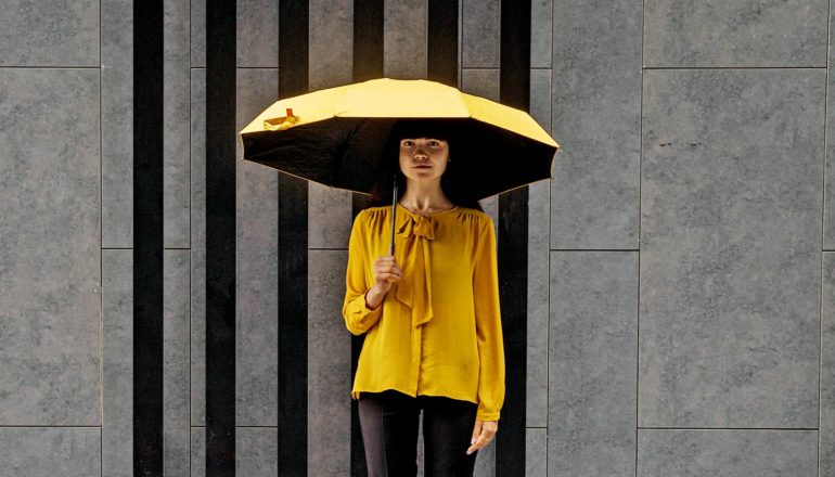 person in yellow stands with yellow umbrella