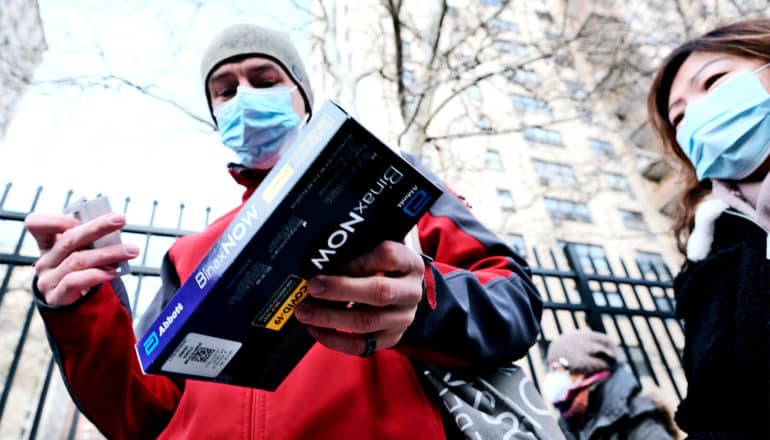 A man holds an at-home COVID-19 test kit while in line outside