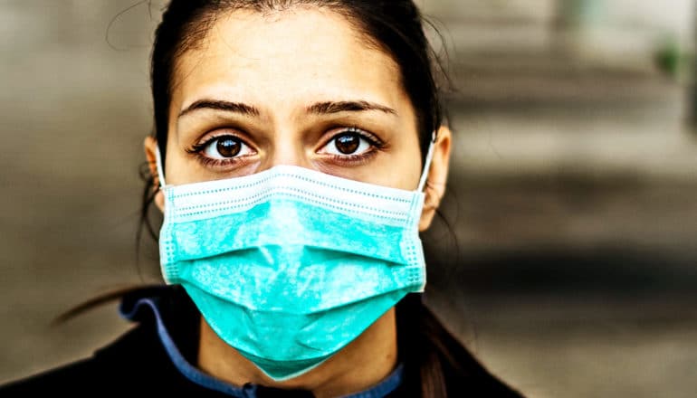 A woman wearing a blue medical mask looks worried