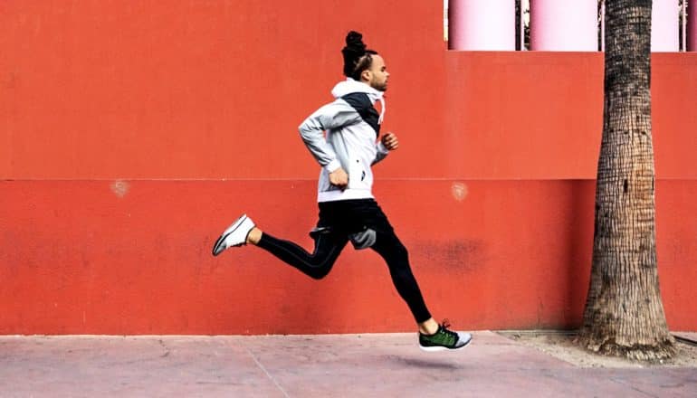 A man runs down a city street past an orange wall