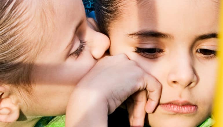 One little girl kisses another's cheek as she looks sad or angry