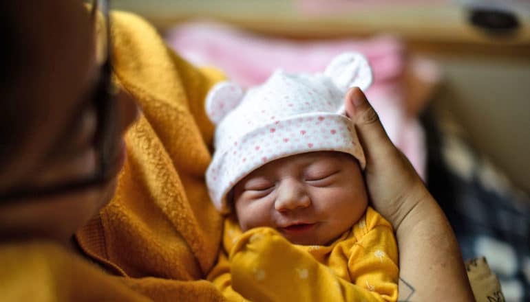 adult holds tiny newborn in hat with ears