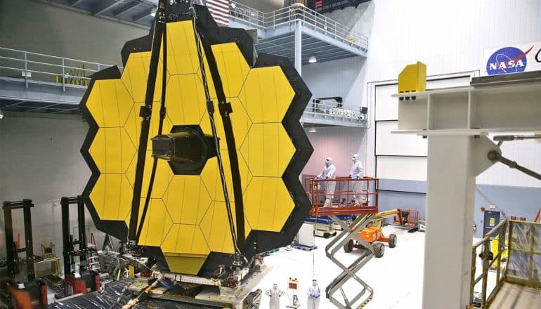 Scientists in white sterile gear work on the gigantic honeycomb-shaped telescope in a large hanger