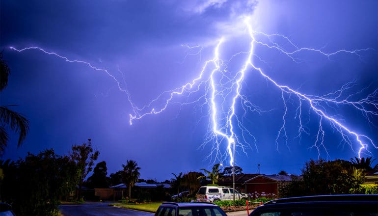 Lightning strikes in a purple sky over some houses