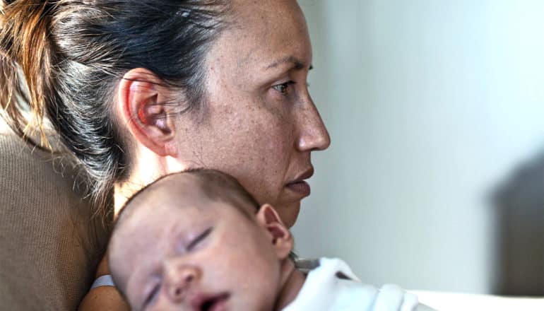 A woman looks into the distance while her baby sleeps on her shoulder