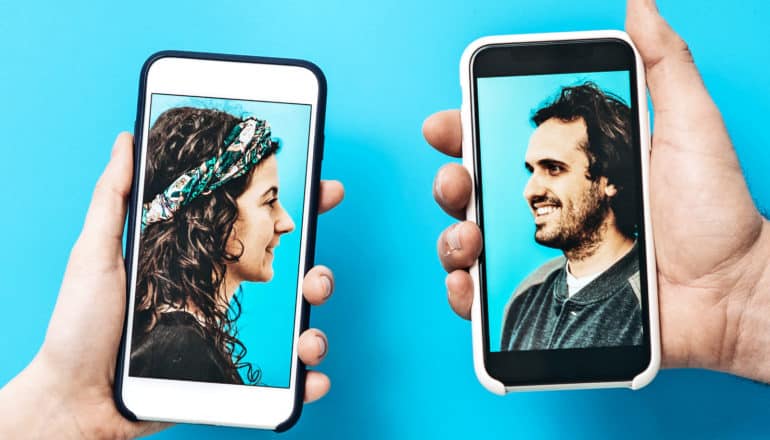 Two people hold smartphones with their faces on the screens looking at each other