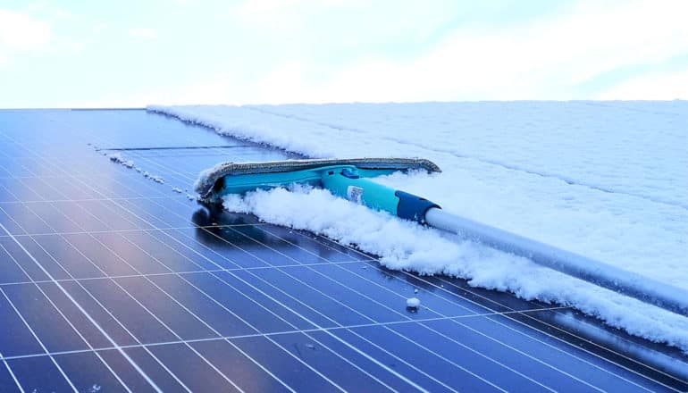 A person uses a scraper to clear snow off solar panels