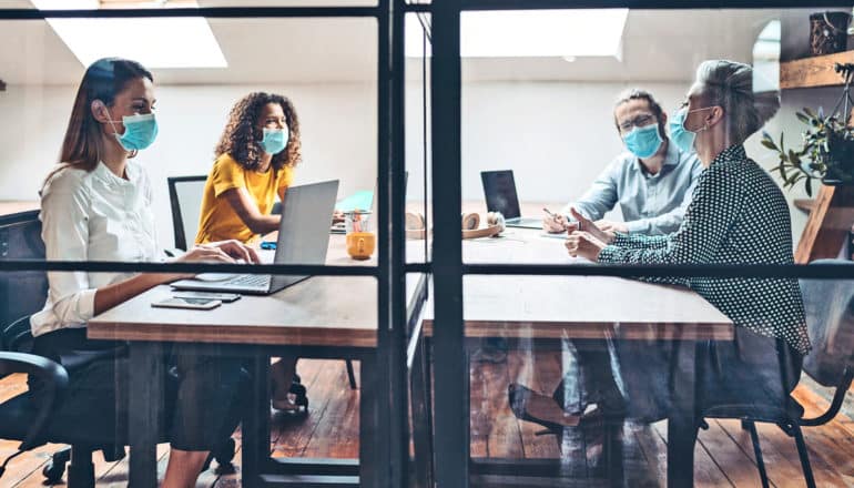 four people at desk behind glass wall