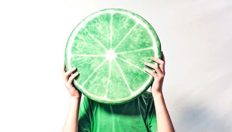 person holds big lime slice in front of face