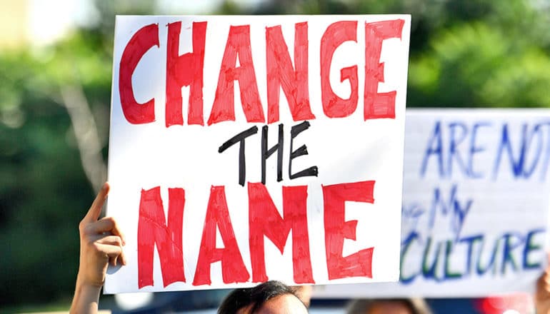 A protester holds a sign that reads "Change the name" in red on a white sign