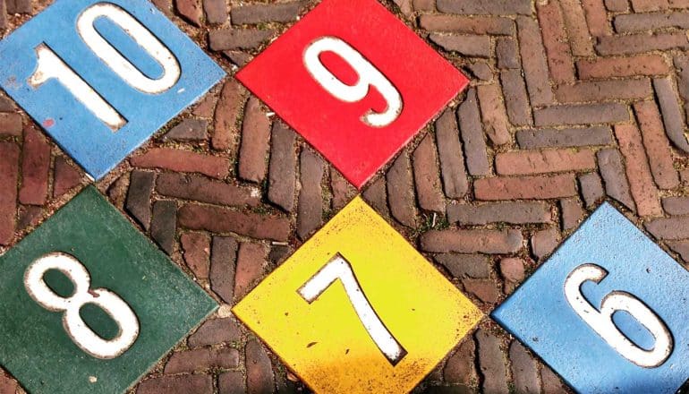 Colorful tiles with numbers 10-6 on them arranged into a hopscotch court set in red bricks