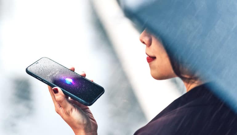 A woman walks with an umbrella in the rain and speaks to her voice assistant on her phone