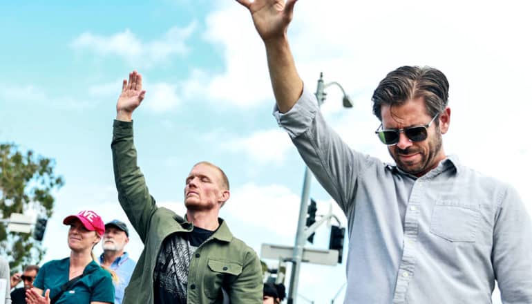 People at an anti-vaccine protest raise their arms and close their eyes