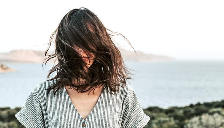 A woman stands on a cliff over the sea as her hair blows in front of her face