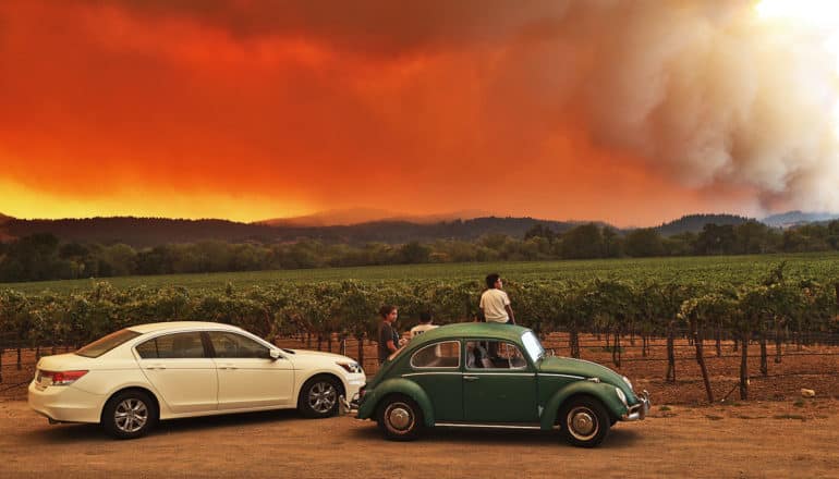 People sit on top of cars while looking at a wildfire on the horizon turn the sky orange