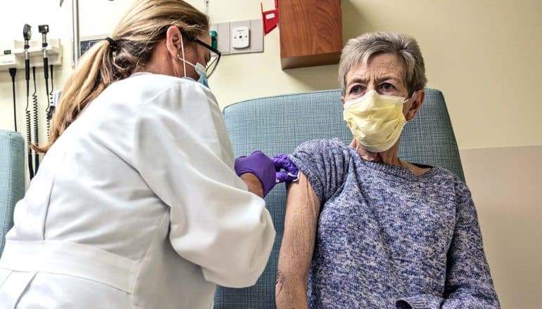 An older woman gets a vaccine while wearing a yellow medical mask