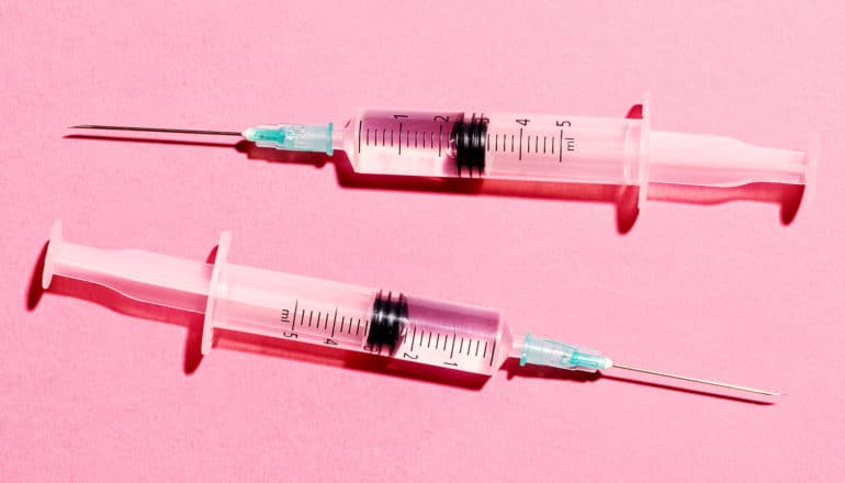 Two syringes sit on a pink background
