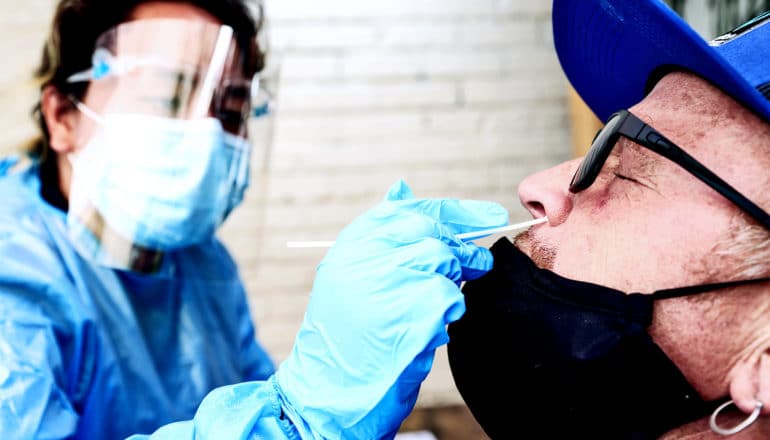 A man gets a nasal swab test from a health worker in protective gear