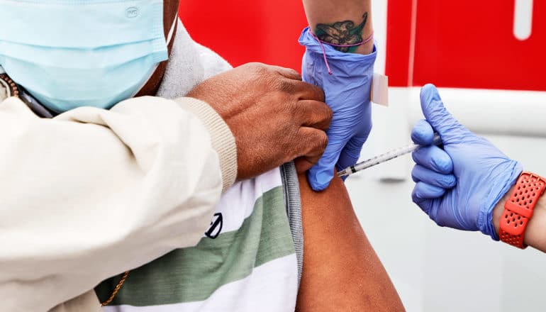 A man gets the Covid vaccine from a health worker wearing purple gloves