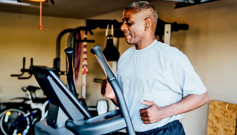 A man runs on a treadmill in his garage while wearing a shirt that reads "Army"