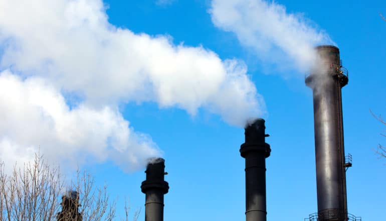 Black smokestacks release white smoke into a blue sky