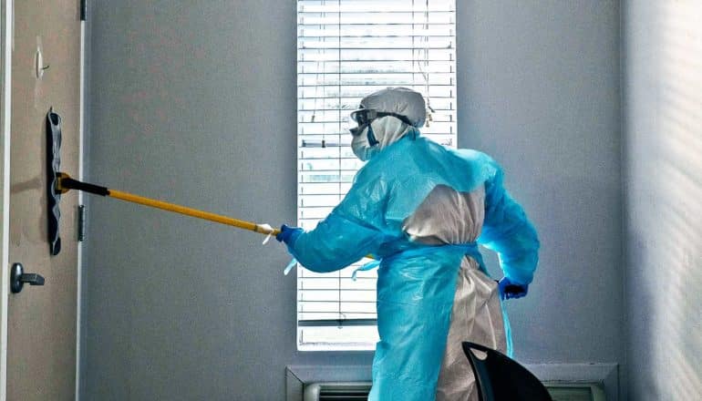 person in hazmat gear uses mop to clean door in hospital room