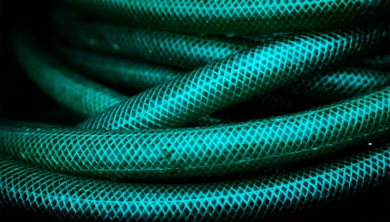 A coiled green garden hose against a dark background