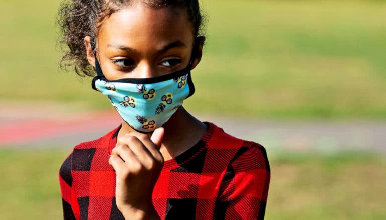 A young girl looks over her shoulder while wearing a face mask