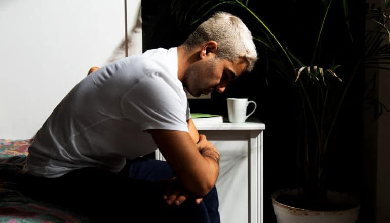 sad person sits on edge of bed