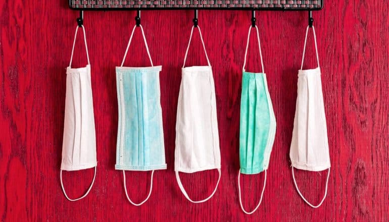 5 masks hang from hooks on a red wood wall