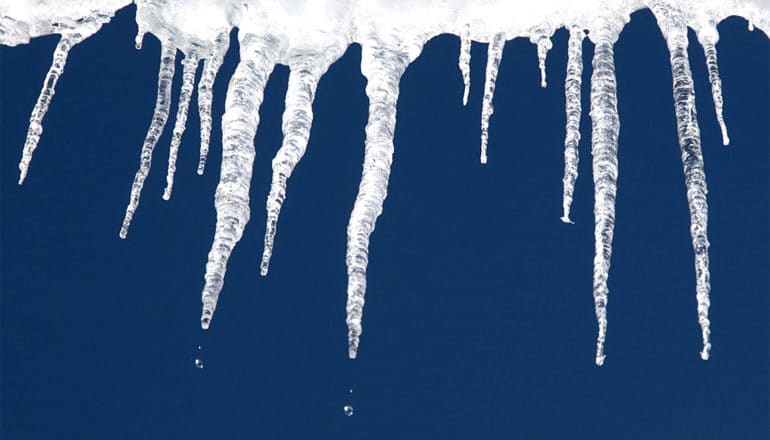 Ice melts off a roof against a blue sky