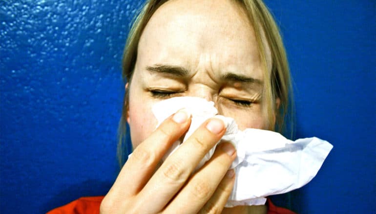 A woman sneezes while holding a tissue up to her nose