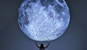 A person stands under a large model of the moon