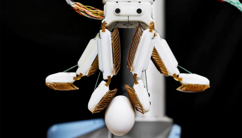 A white four-fingered robot hand holds an egg between two fingers