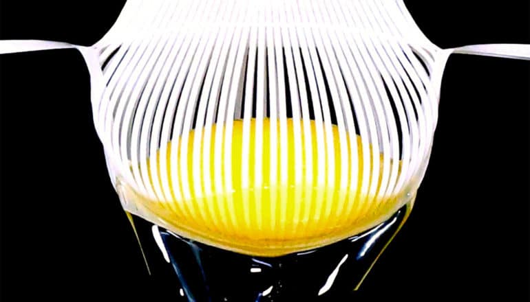 The robotic gripper holds an egg yolk with many tiny strands as the egg white falls through its grasp